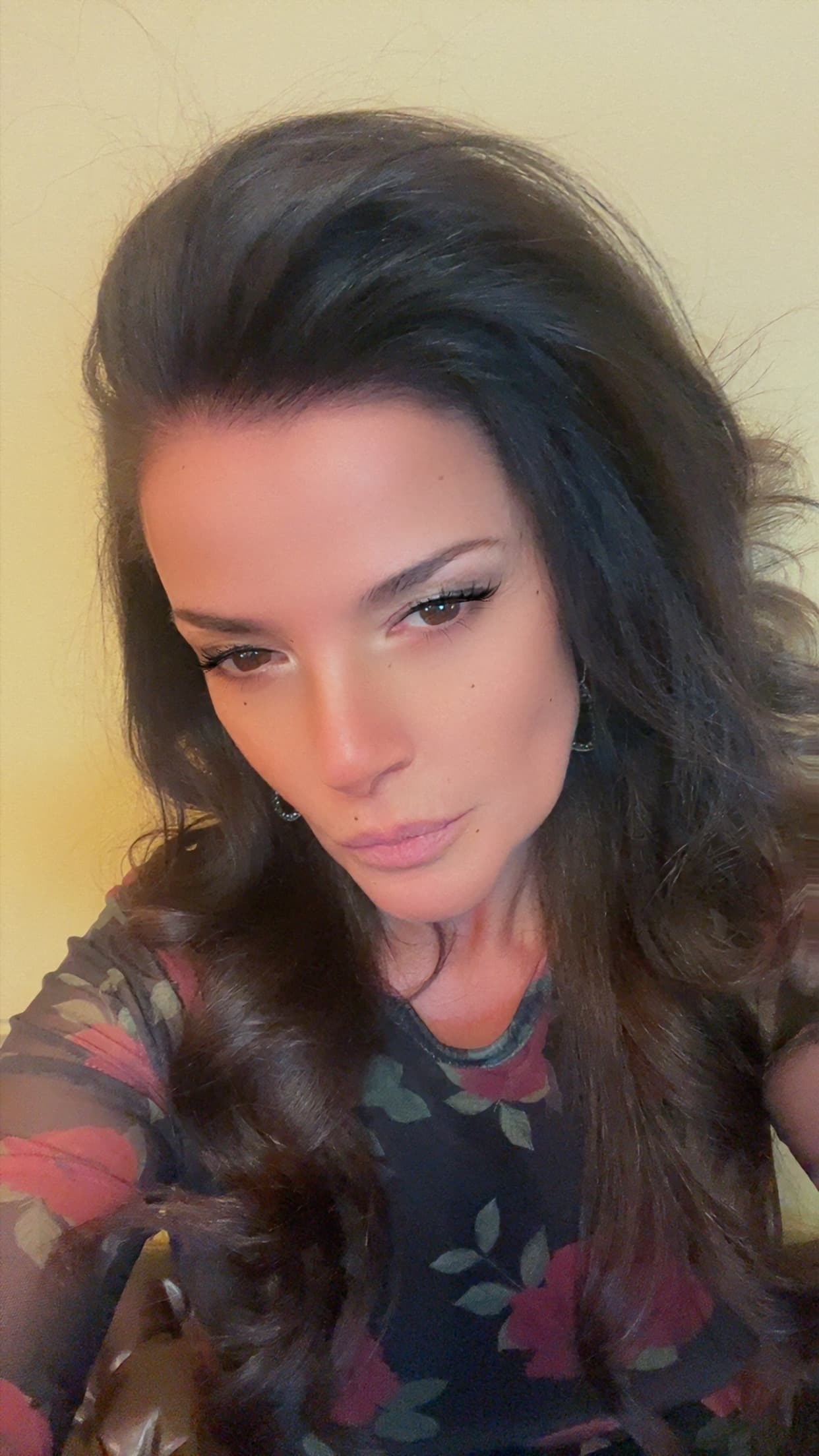 Woman with long dark wavy hair and a floral top looking seriously at the camera.